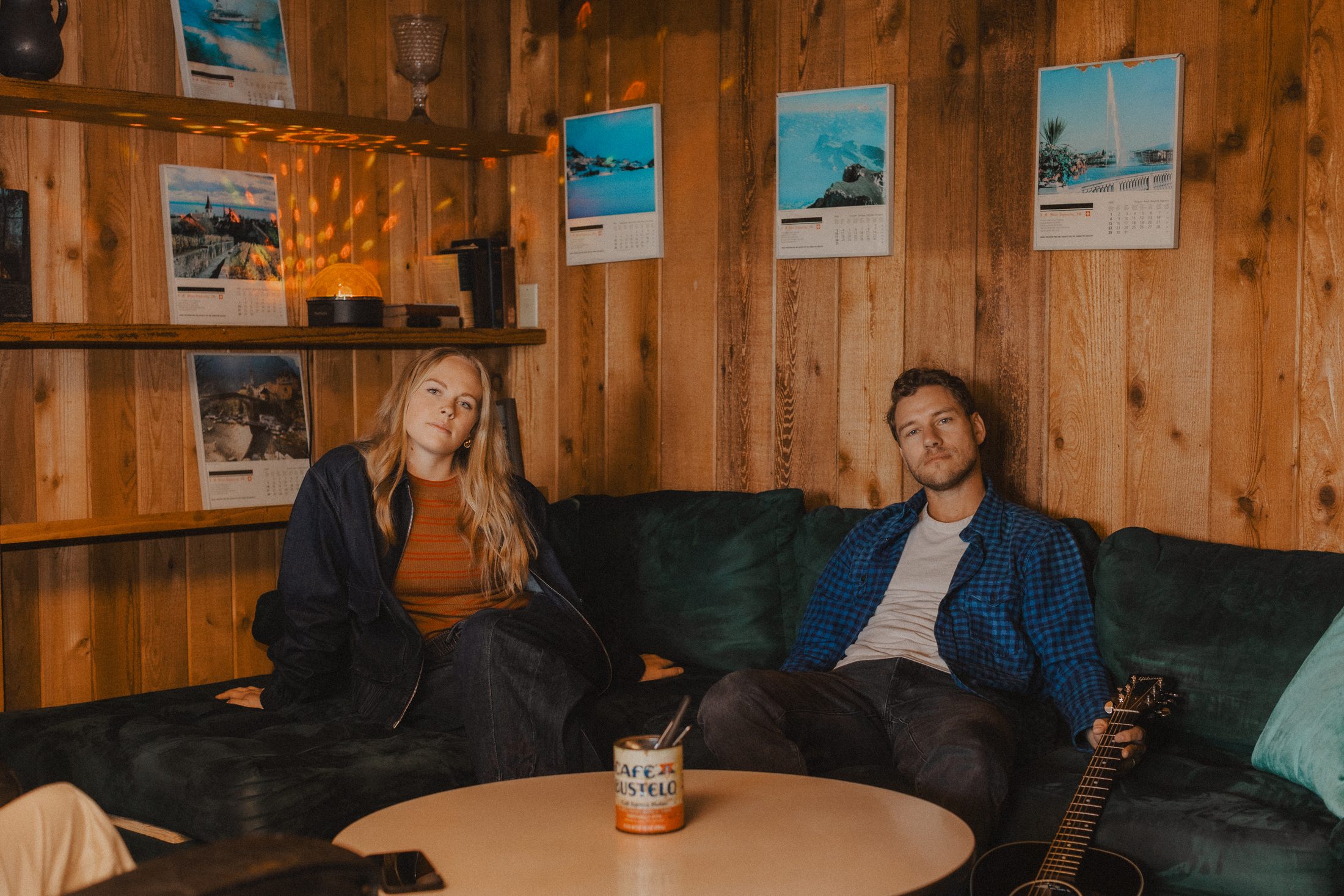 Kadi Zabka and Brian Albright of Salt seated on a green velvet couch in a wood-panelled room, an acoustic guitar beside him.
